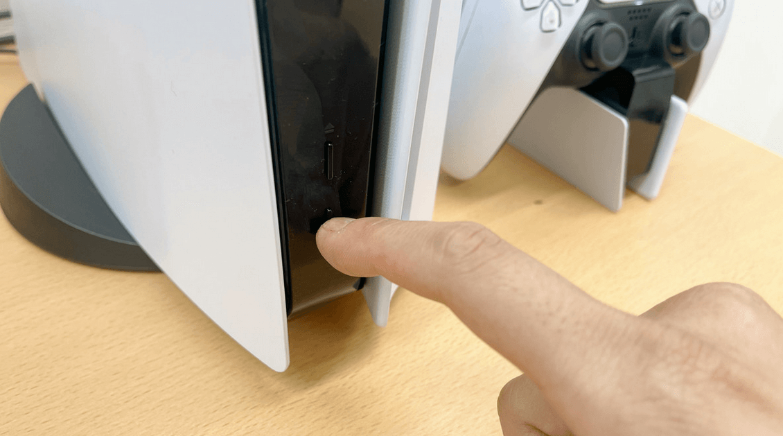 A finger pressing the PS5 power button
