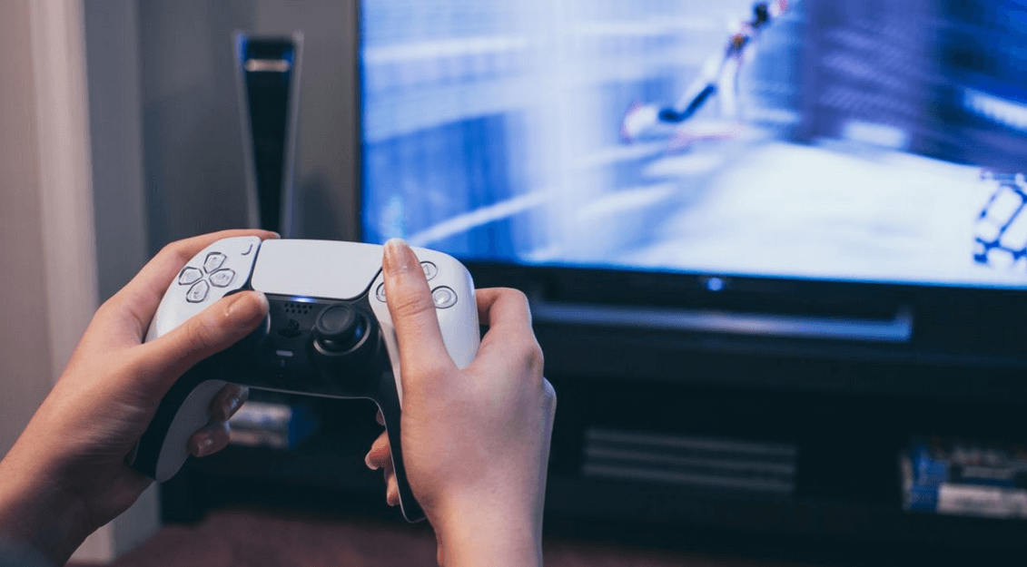 two hands holding PS5 controller infront of a screen